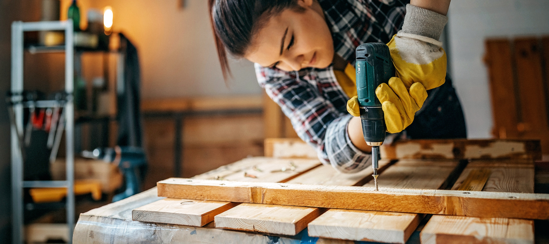 Woman using a power drill on wood structure inside of a garage
